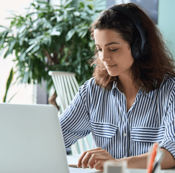 Mujer usando audífonos y mirando su computadora portátil