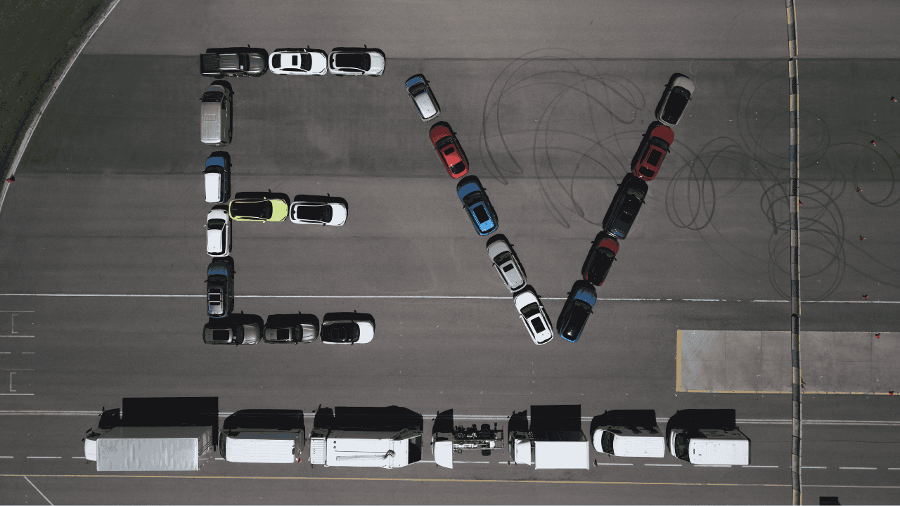 Toma área de varios vehículos alineados formando la palabra "EV DAY" sobre una pista de manejo. Toma área de varios vehículos alineados formando la palabra "EV DAY" sobre una pista de manejo.